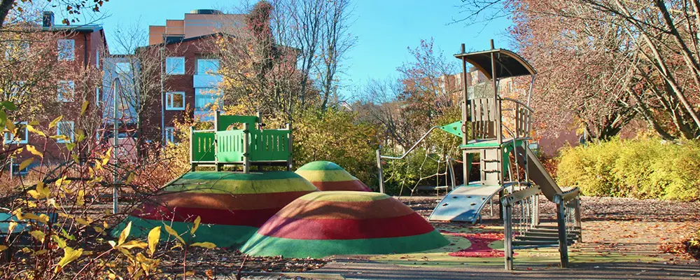 Foto på en lekplats där man ser balansgång, klätterställning, rutschkanor och färgglada gummikullar.